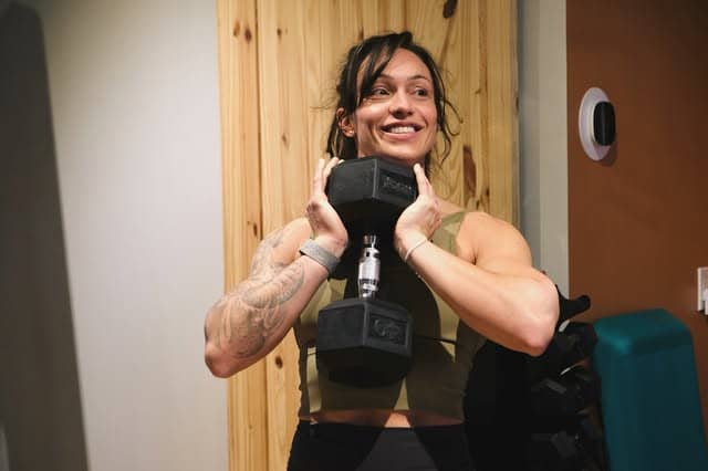 A member smiling mid set with a dumbbell at Bar None Fitness Studio in Burlington